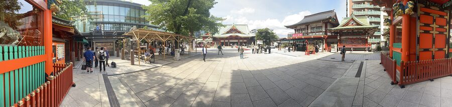 A wide panoramic view of Kanda Myojin shrine grounds with red lanterns, stone gates, and visitors.