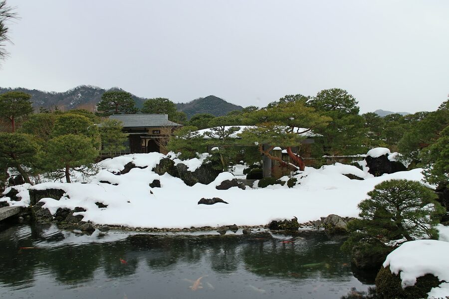 The Adachi garden framed as a living painting through a sliding window in winter