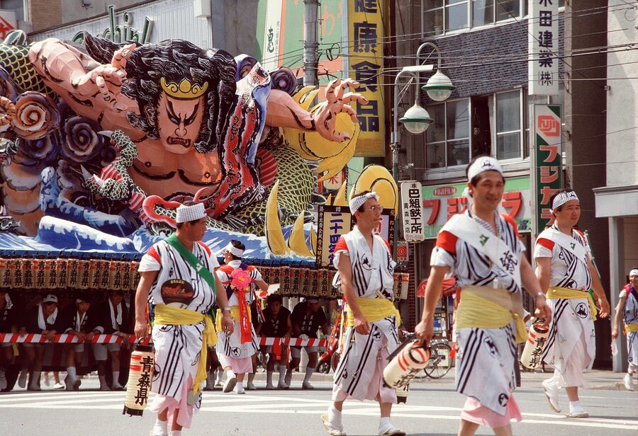 A wide street view of Nebuta from 1985, floats in slow procession past several thousand spectators.