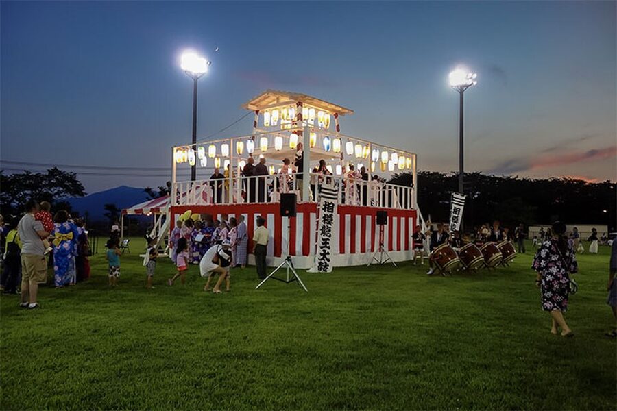 A wooden yagura tower with drummers on top and dancers circling at the base during a Bon Odori festival