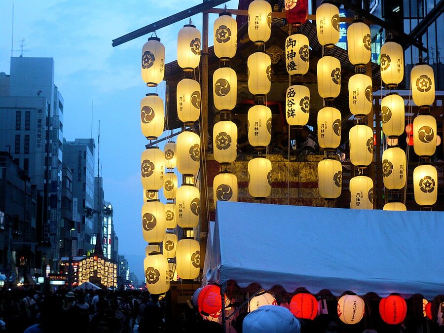 Yoiyama evening crowd filling street around lantern-lit yamaboko float during Gion Matsuri