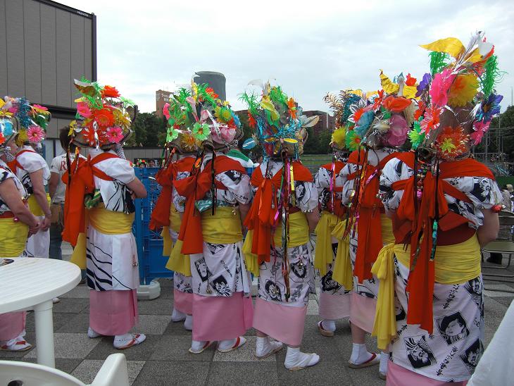 A haneto dancer in traditional yukata, kasa hat, and waist bells, ready to jump and shout the Rassera chant.