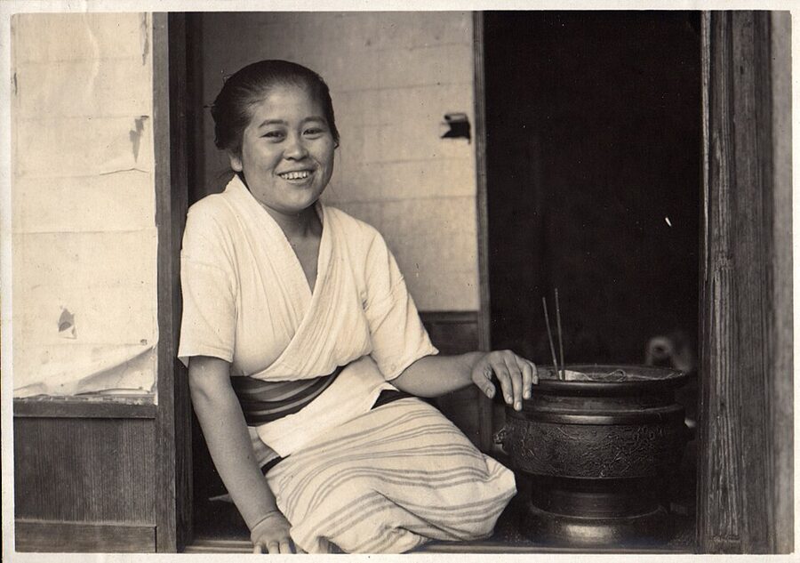 1915 photograph by Elstner Hilton of a Japanese woman in kimono warming her hands over a hibachi brazier
