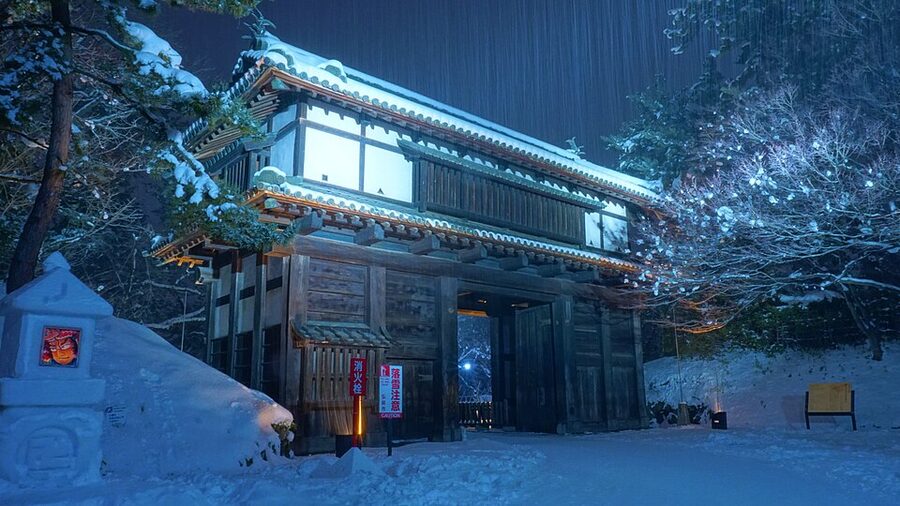 Minami-uchimon Gate the south entrance to the Ninomaru bailey at Hirosaki Castle photographed at night with cherry blossoms illuminated behind the gatehouse