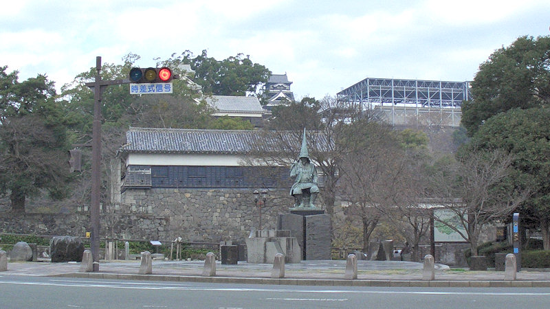 The large bronze statue of Kato Kiyomasa in full armour standing in front of Kumamoto Castle walls