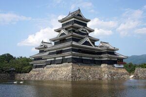 Matsumoto Castle daitenshu black lacquered six-story tenshu reflected in the inner moat with the connected inui-ko-tenshu and watari-yagura visible beside it