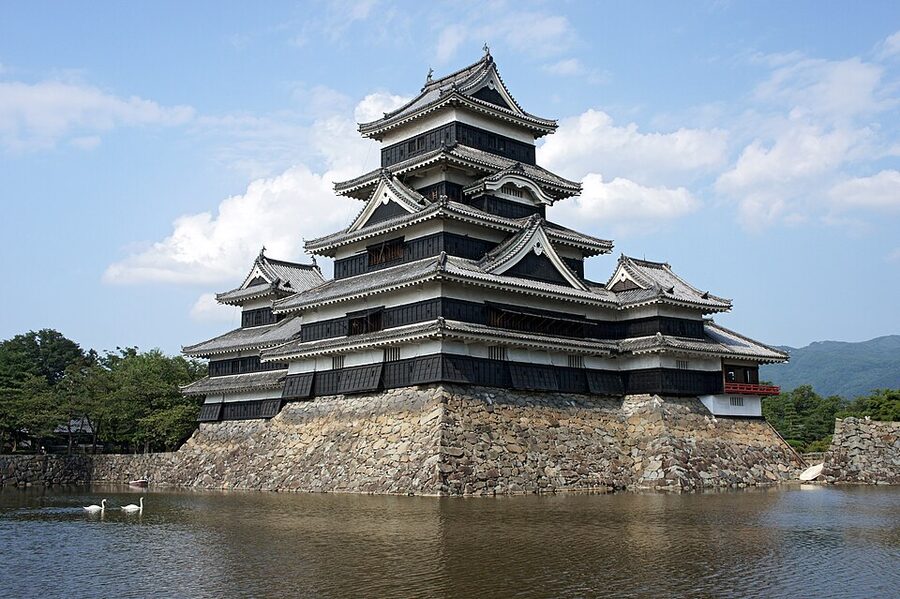 Matsumoto Castle daitenshu black lacquered six-story tenshu reflected in the inner moat with the connected inui-ko-tenshu and watari-yagura visible beside it
