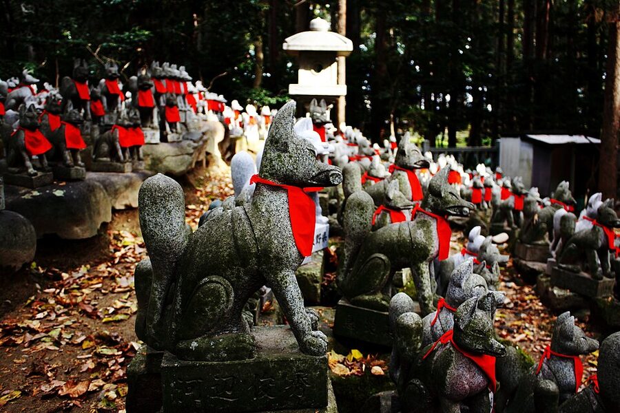 Detailed close-up of fox statues wearing red bibs at Reiko-zuka